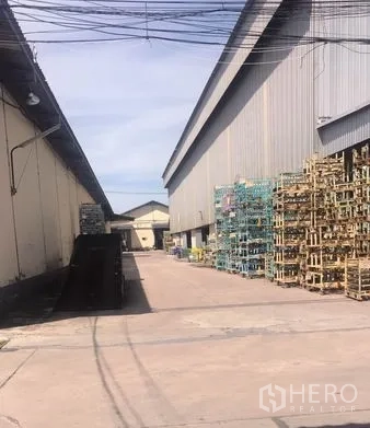 货栈 出租在Chachoengsao - 仓库旁服务场地，堆放金属货架，硬化地面便于车辆调头。