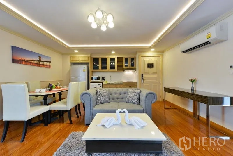 房间 出租在Khlong Toei, Bangkok - 开放式客厅，沙发、餐桌与小厨房，天花灯带营造氛围。