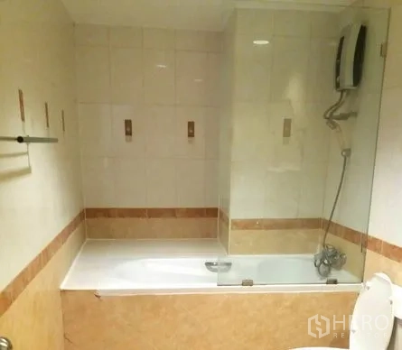 Condominium for rent in Watthana, Bangkok - Tiled bathroom featuring a bathtub with glass screen, handheld shower and water heater.