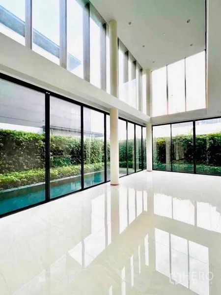 独立式住宅 出售在Huai Khwang, Bangkok - 采光充足的双层挑高会客区，窗外即泳池与花园。