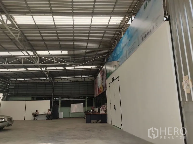 Warehouse for rent in Bueng Kum, Bangkok - Spacious steel-frame warehouse interior in Bueng Kum with high ceiling, skylights, concrete floor and a partitioned office or cold-room door.