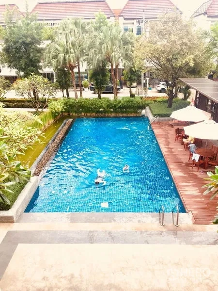 联排别墅 出租在Prawet, Bangkok - 室外游泳池，旁有木平台、绿化与遮阳伞