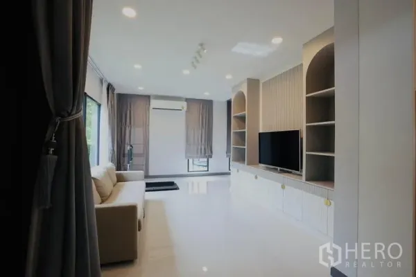 独立式住宅 出租在Bang Phli, Samut Prakan - 宽敞家庭厅，内置电视柜与开放式搁架，灰色窗帘。