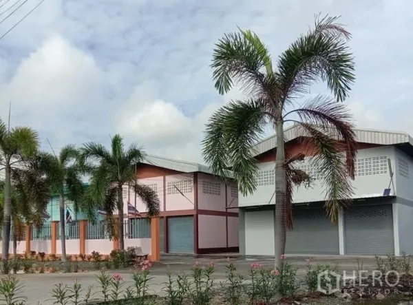 Factory for rent in Lat Lum Kaeo, Pathum Thani - Landscaped factory buildings with colorful facades, palm trees, and flowering borders inside the compound.