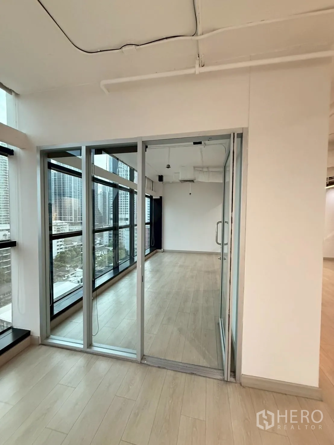 办公室 for rent in Watthana, Bangkok - 玻璃隔断房间，临近落地窗与浅木纹地面。