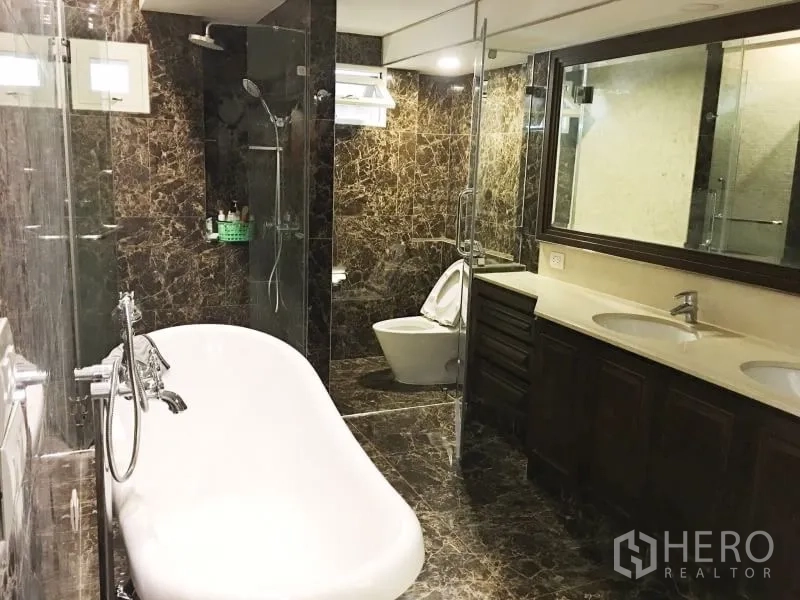 Detached House for rent in Khlong Toei, Bangkok - Luxurious bathroom with freestanding bathtub, double vanity and glass-enclosed rain shower in dark marble.