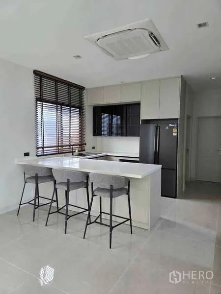 Detached House for rent in Bang Phli, Samut Prakan - Bright kitchen with island breakfast bar, built-in cabinets and a black refrigerator.