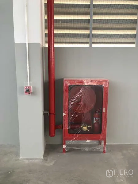 Factory for rent or sale in Samut Prakan - Red fire hose cabinet and sprinkler pipe installed along the wall.
