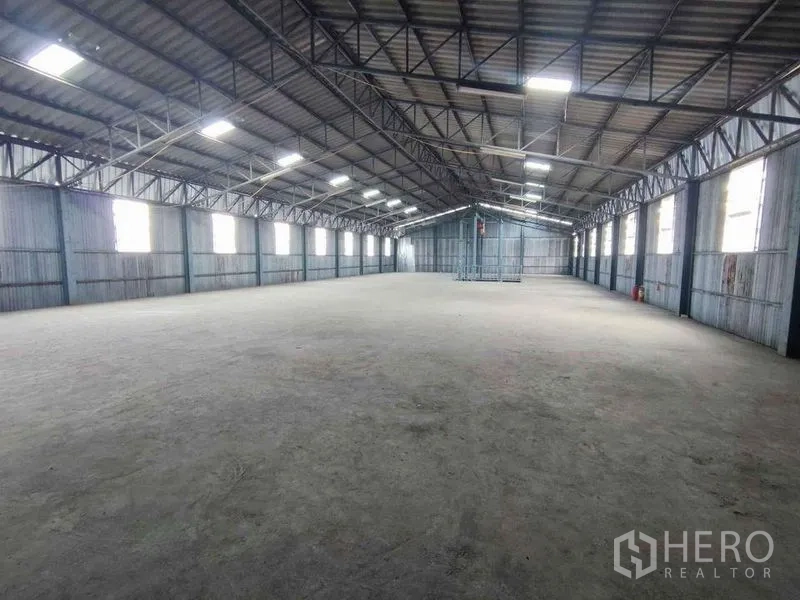 Warehouse for rent in Samut Sakhon - High clear-span warehouse hall with steel truss roof and side windows providing natural light.