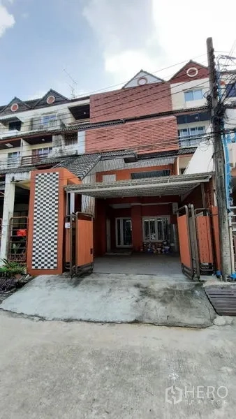Townhouse for rent or sale in Suan Luang, Bangkok - Front driveway and wide carport with folding wooden gates.
