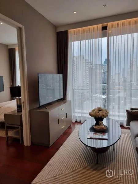 คอนโด ให้เช่าในWatthana, Bangkok - มุมนั่งเล่นพร้อมตู้วางทีวีข้างหน้าต่าง โต๊ะกลางทรงรีและวิวเมือง มีทางเข้าห้องนอนให้เห็น