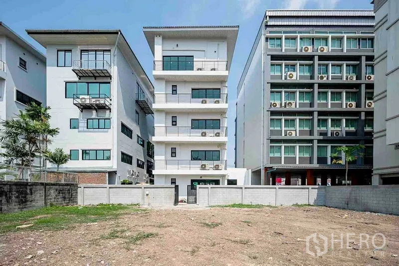 带办公室的家 出租在Suan Luang, Bangkok - 建筑后立面，夹在邻近办公楼之间，前方是围合的庭院空地。