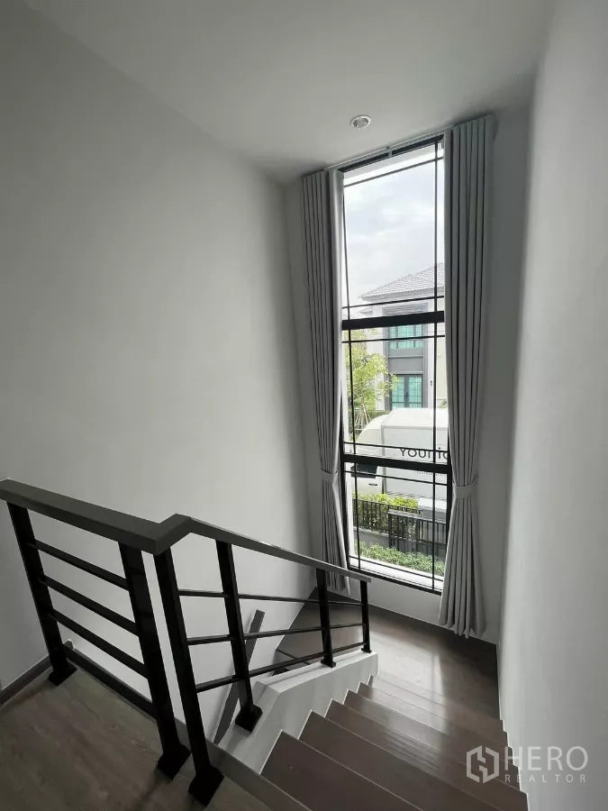 Detached House for rent or sale in Bang Phli, Samut Prakan - Staircase illuminated by a tall floor-to-ceiling window with curtains.