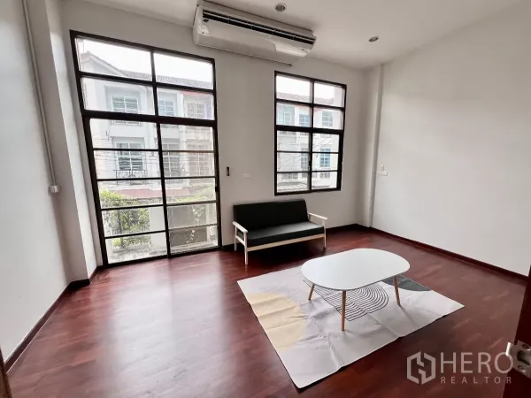 Townhouse for rent or sale in Phra Khanong, Bangkok - Living area with floor-to-ceiling windows, wood floors, sofa and white coffee table.