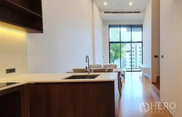 Condominium for sale in Watthana, Bangkok - Modern L-shaped kitchen facing a bright living room with floor-to-ceiling windows and city view.