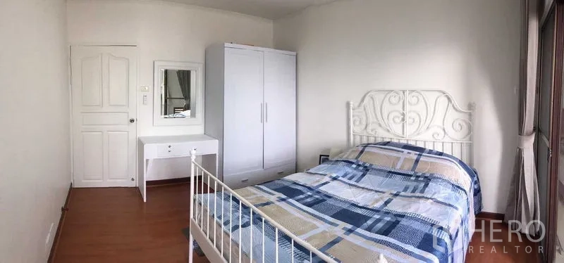 Condominium for rent or sale in Din Daeng, Bangkok - Sunlit bedroom with white wrought-iron bedframe, wardrobe and dressing table over warm wood floors.