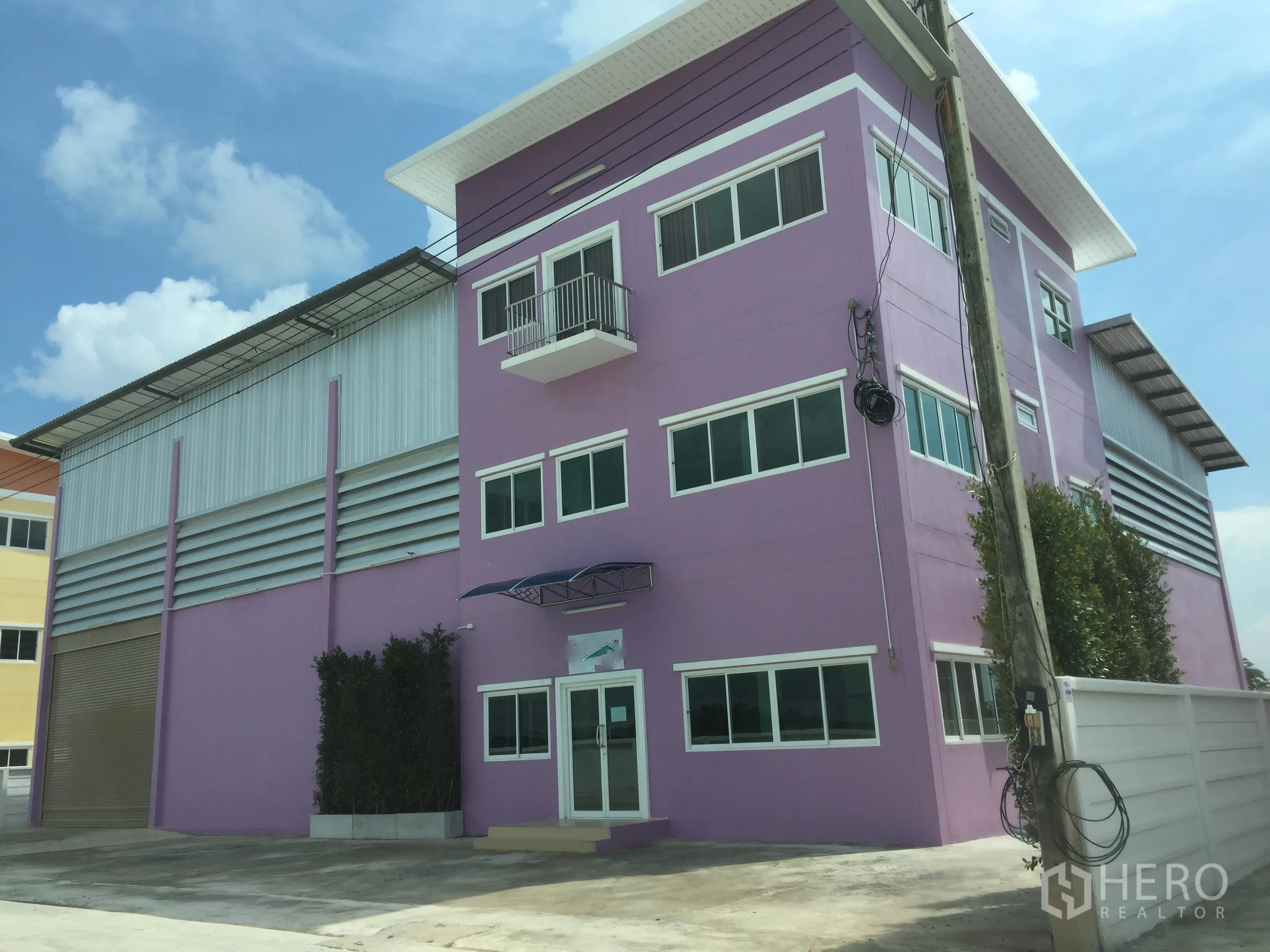 Factory for rent in Pathum Thani - Purple three-storey office attached to a steel-clad factory with a large roller shutter and wide concrete loading yard in Khlong Luang.