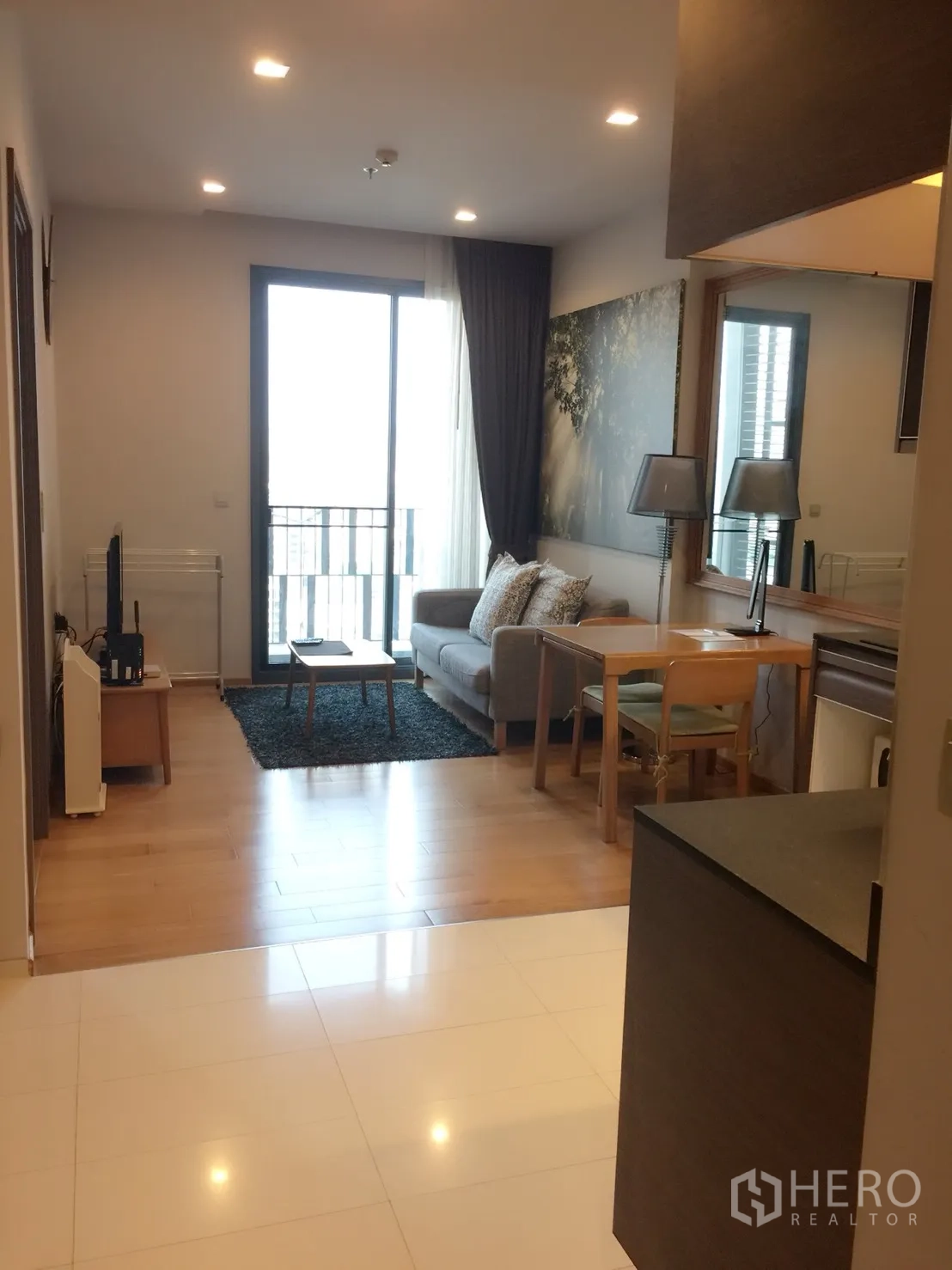 Condominium for rent in Khlong Toei, Bangkok - Open-plan living and dining area with recessed lights and a balcony accessed by sliding glass doors.
