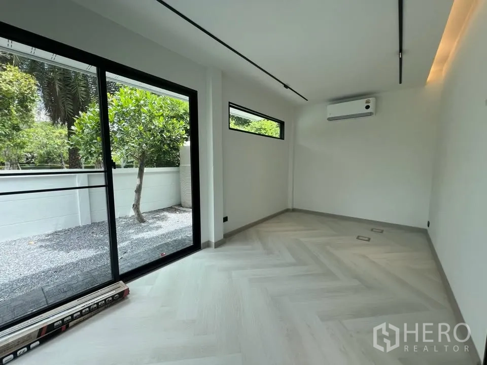 联排别墅 for rent in Prawet, Bangkok - 明亮房间，推拉门通往碎石庭院，墙挂空调可见。