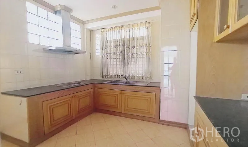 独立式住宅 出售在Bang Kapi, Bangkok - L形厨房，木质柜体、灶台与烟机，配窗帘与采光窗。