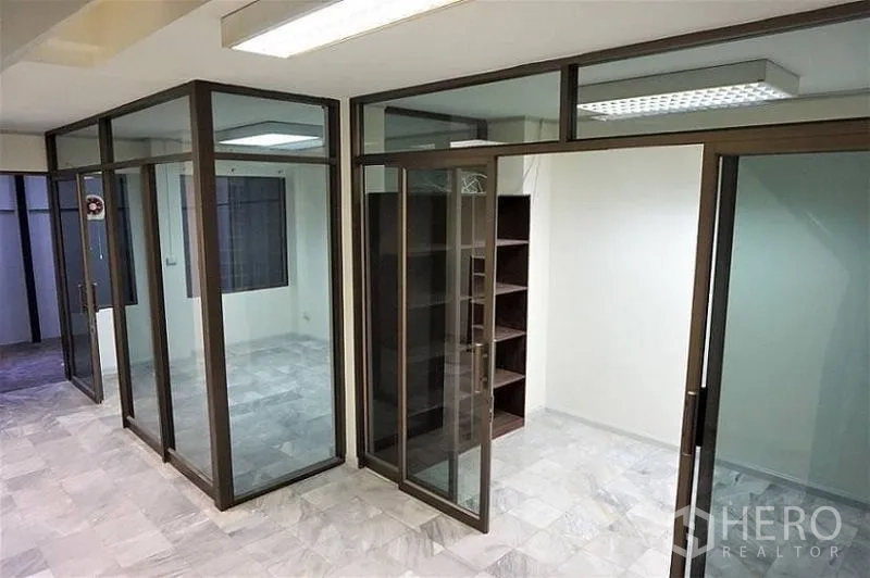 Home Office for rent in Khlong Toei, Bangkok - Private meeting rooms created with full-height glass partitions and shelving under fluorescent lighting.