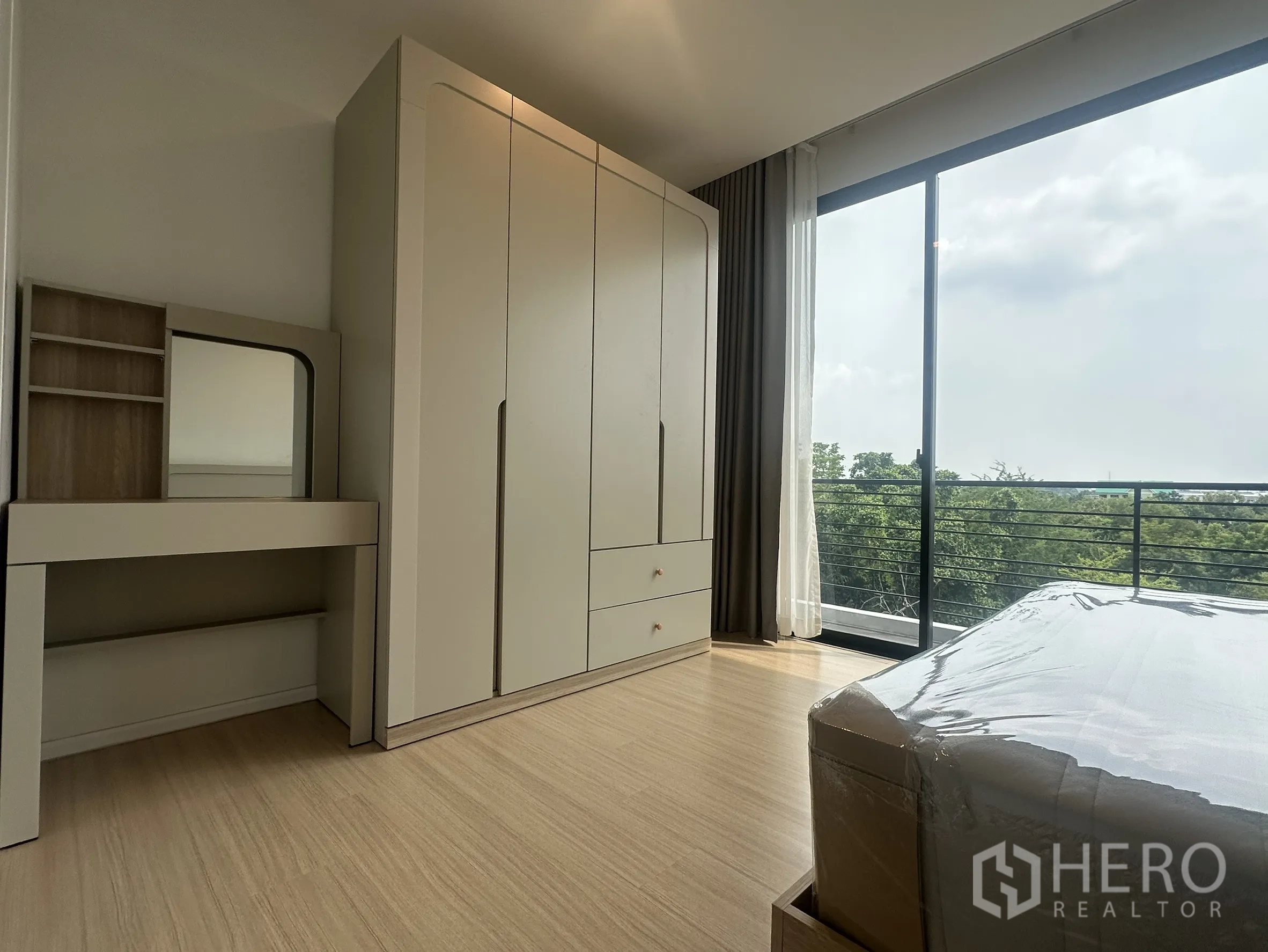 Townhouse for rent in Suan Luang, Bangkok - Bedroom with wardrobe and dressing table opening to a balcony with green views.