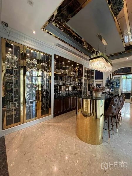 独立式住宅 出租或出售在Thawi Watthana, Bangkok - 奢华家用吧台，金色岛台、玻璃展示柜与皮质高脚椅。