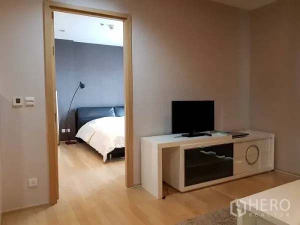 Condominium for rent in Khlong Toei, Bangkok - Bright living area with TV console and doorway to the bedroom, featuring light wood flooring.