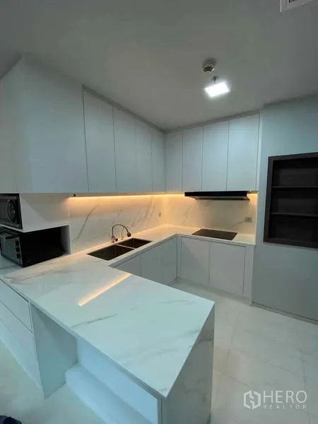 Condominium for rent or sale in Khlong Toei, Bangkok - Contemporary kitchen with induction cooktop, built-in cabinetry and marble surfaces.
