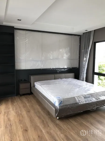 Detached House for rent in Bang Kapi, Bangkok - Primary bedroom with wood flooring, large windows and upholstered headboard wall.