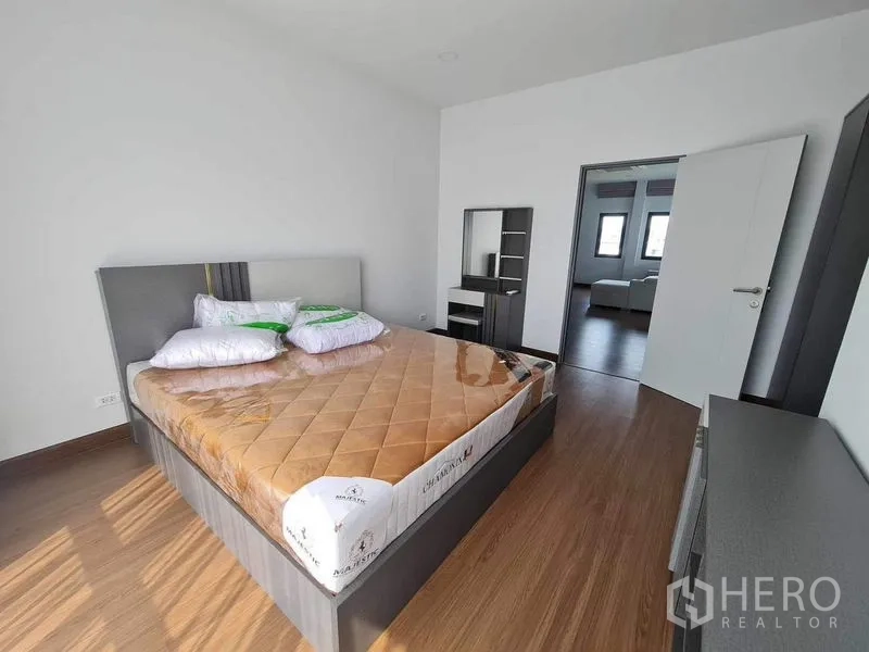 Detached House for rent or sale in Bang Phli, Samut Prakan - Alternate angle of bedroom featuring wood flooring and vanity near open doorway.