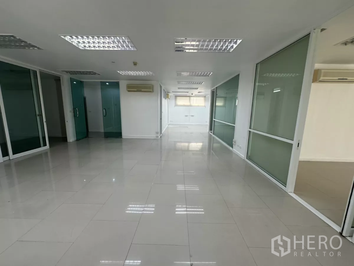 Office Space for rent in Huai Khwang, Bangkok - Hallway view of the office with several glass-partitioned rooms and white tile floors.