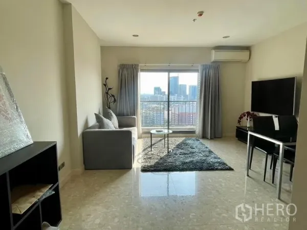 Condominium for sale in Khlong Toei, Bangkok - Living room with sofa and dining table opening to a balcony overlooking the city.
