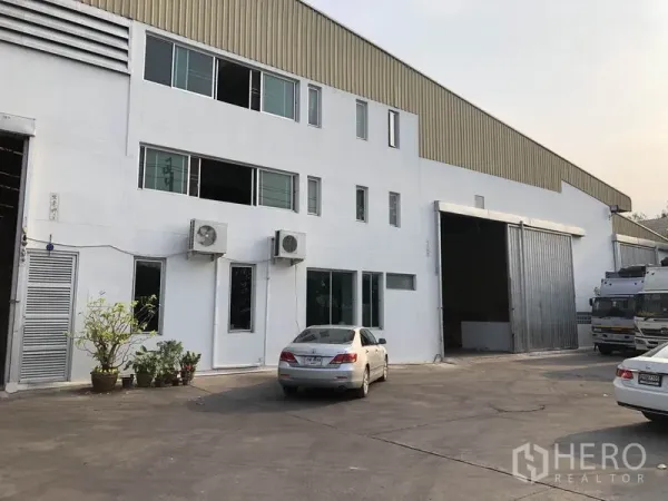 Factory for rent in Bang Bua Thong, Nonthaburi - Two-storey factory exterior in Bang Bua Thong with large sliding warehouse door and on-site parking.