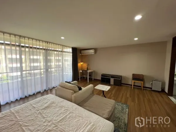 Townhouse for rent or sale in Suan Luang, Bangkok - Bright bedroom with a long curtain wall, lounge seating, desk and wood flooring.