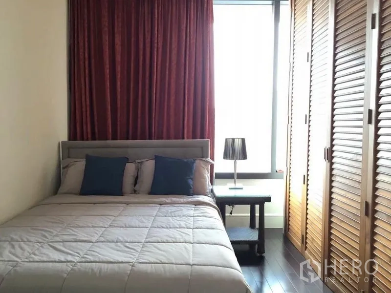 Condominium for rent in Khlong Toei, Bangkok - Second bedroom with double bed, floor-to-ceiling wardrobes and red curtains.