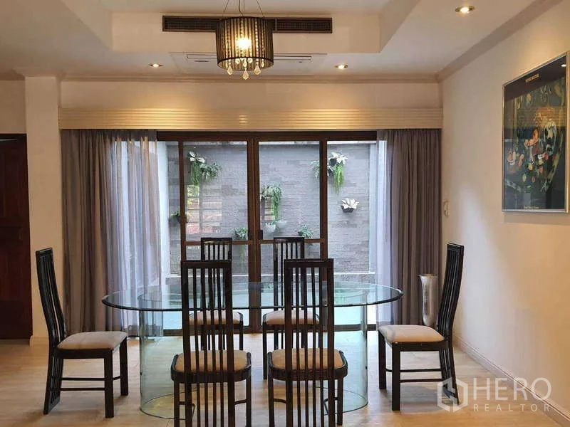 Townhouse for rent in Khlong Toei, Bangkok - Dining room with oval glass table, six chairs and sliding doors to patio wall planters.