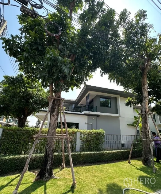 Detached House for sale in Lam Luk Ka, Pathum Thani - Corner plot exterior with green lawn, tall trees and a side view of the house.