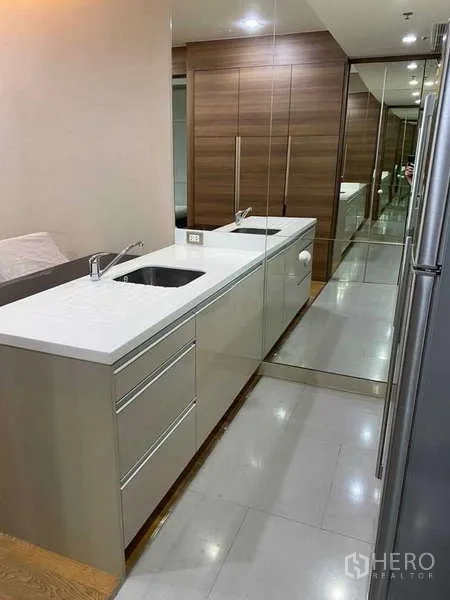 Condominium for rent in Bang Rak, Bangkok - Long galley kitchen with double sinks and mirrored backsplash.