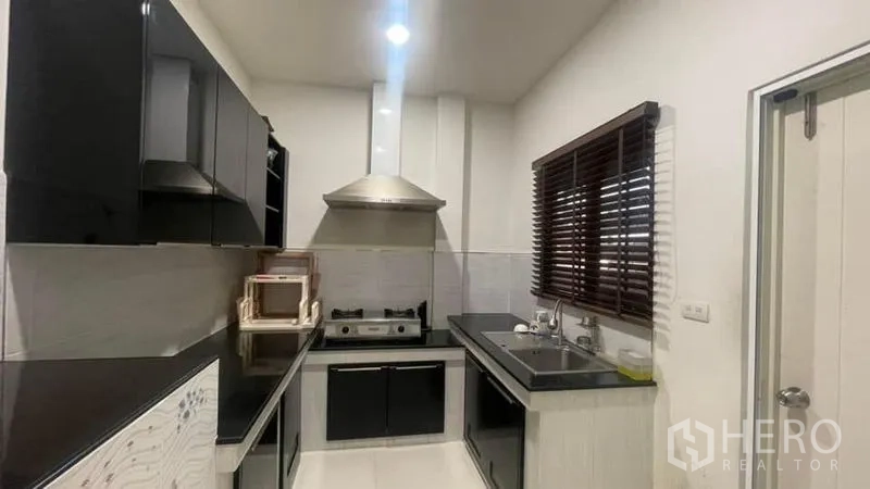 Detached House for rent or sale in Prawet, Bangkok - Fitted galley kitchen with black cabinetry, gas hob, hood and double sink.