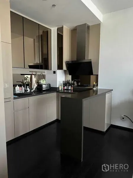 Condominium for rent in Khlong Toei, Bangkok - Modern L-shaped kitchen with glossy cabinets, peninsula counter and range hood.