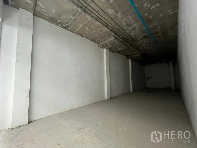 Retail Space for rent in Khlong Toei, Bangkok - Side view of a plain wall and ceiling with blue utility pipe in an unfinished unit.