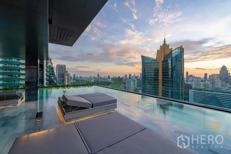 Condominium for rent in Watthana, Bangkok - Rooftop infinity pool deck with loungers and panoramic city views at sunset.