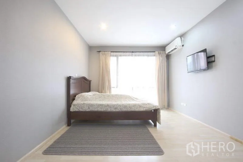 Townhouse for sale in Suan Luang, Bangkok - Second bedroom with wall-mounted TV, air conditioner, and wide window.