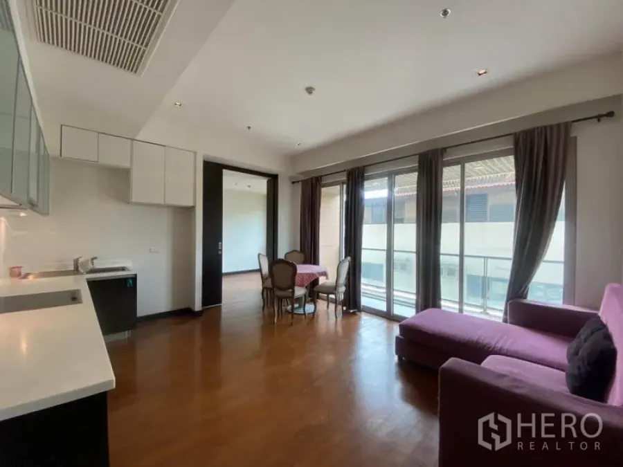 公寓 出租在Yan Nawa, Bangkok - 明亮的开放式客厅，木地板、紫色沙发、餐桌与通向阳台的落地窗。