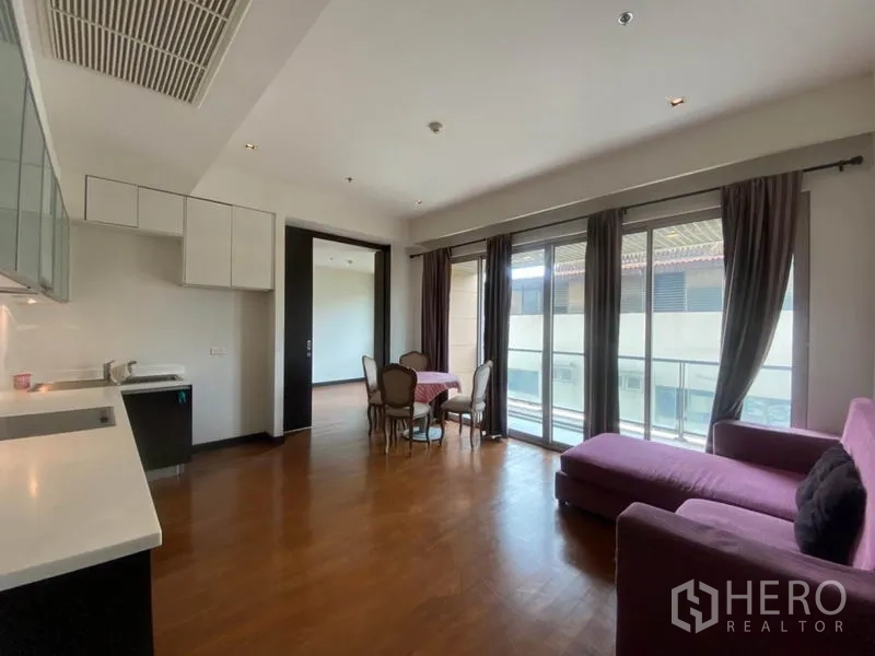 公寓 出租在Yan Nawa, Bangkok - 明亮的开放式客厅，木地板、紫色沙发、餐桌与通向阳台的落地窗。