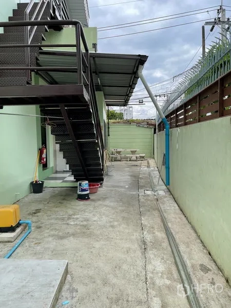 Warehouse for rent in Khan Na Yao, Bangkok - Exterior metal staircase and side service passage along a secure boundary wall.