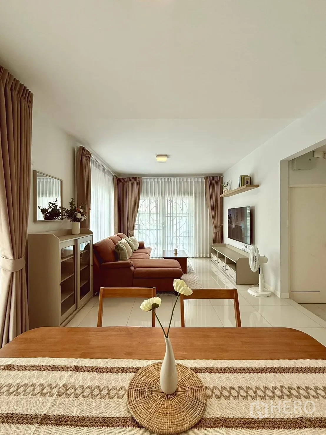 Detached House for rent in Bang Phli, Samut Prakan - Dining table with decorative runner facing a lounge with sectional sofa and bright windows.