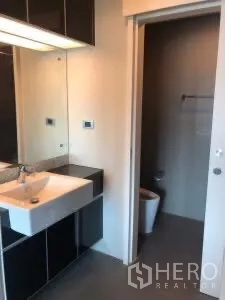 Condominium for rent or sale in Khlong Toei, Bangkok - Bathroom vanity with large mirror, sink and sliding door to the toilet area.