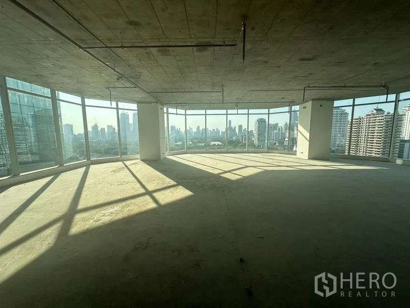 Office Space for rent in Watthana, Bangkok - Corner open-plan office with floor-to-ceiling windows and panoramic Bangkok skyline views, unfinished concrete ceiling and floors.
